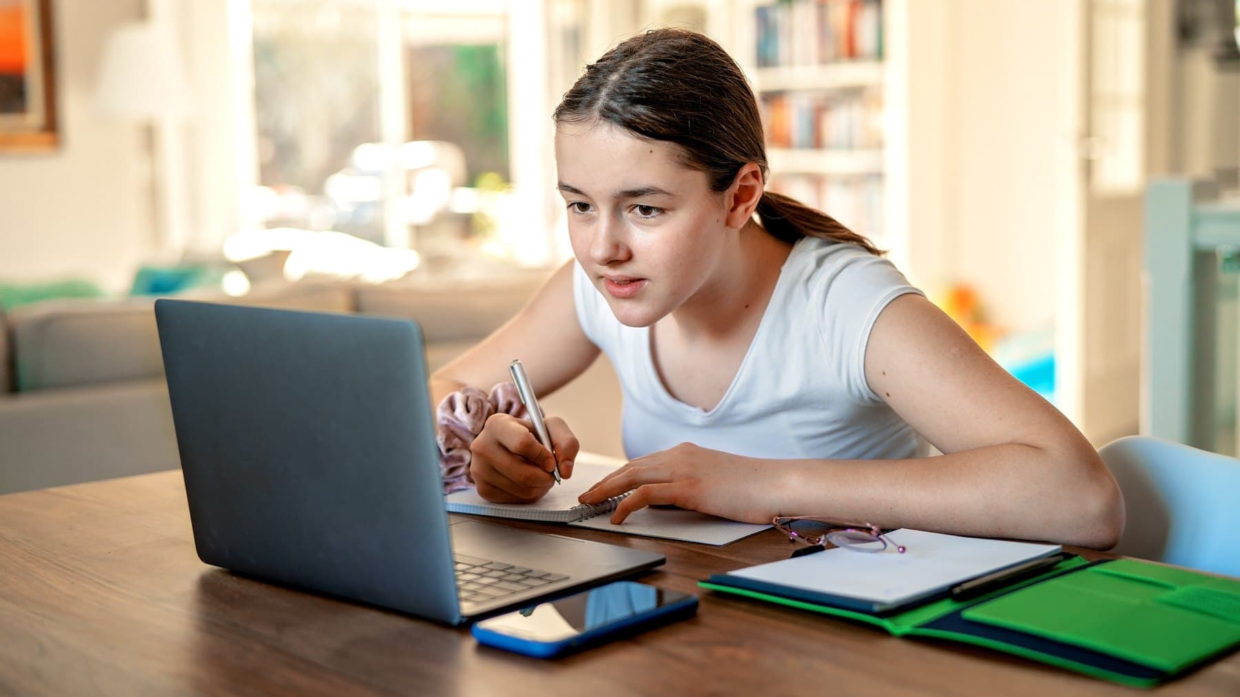 A Prep School pupil working at her laptop at home, notes and folders spread across the table